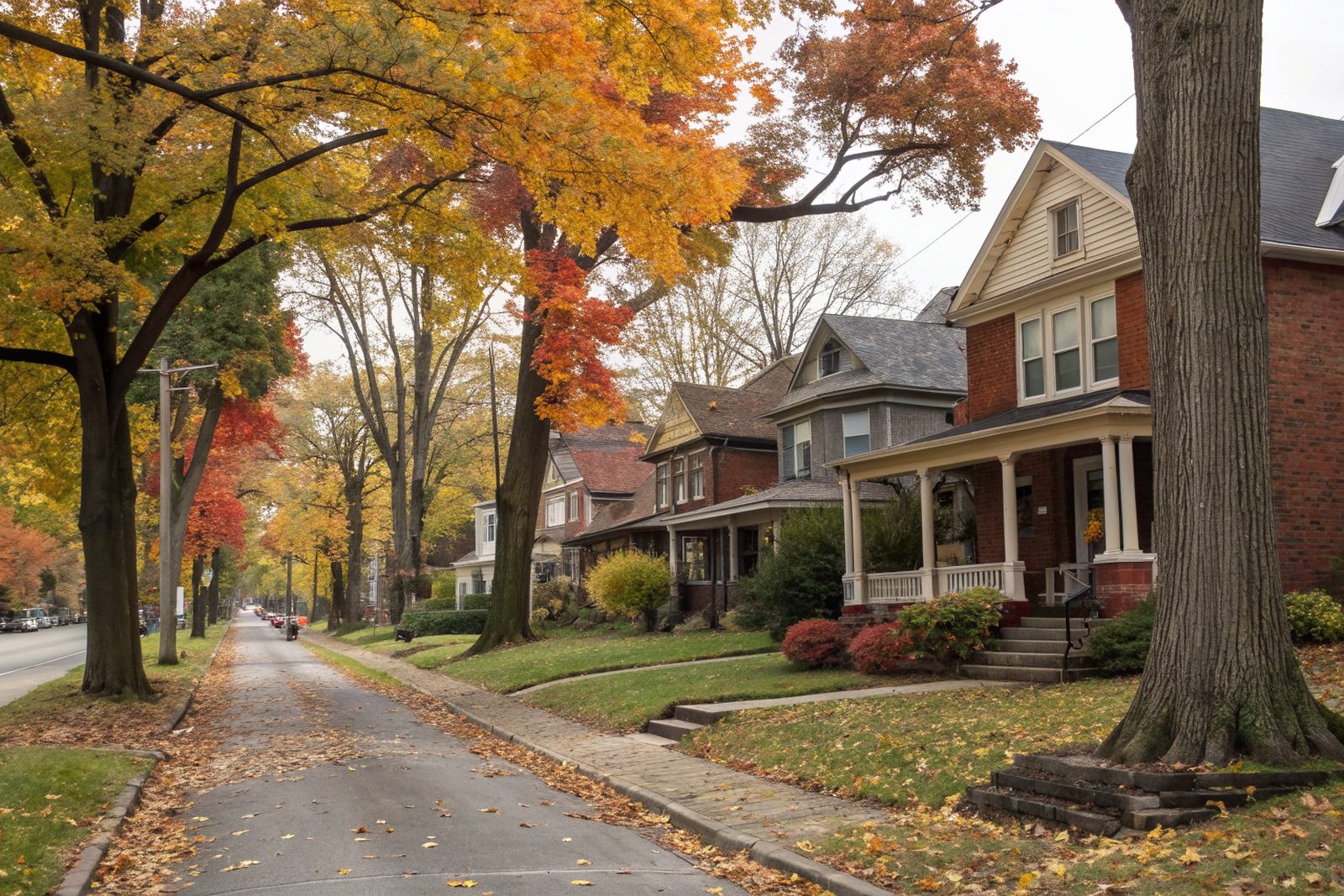 A tree-lined street of older brick and frame houses with gabled shingle roofs and front porches in autumn